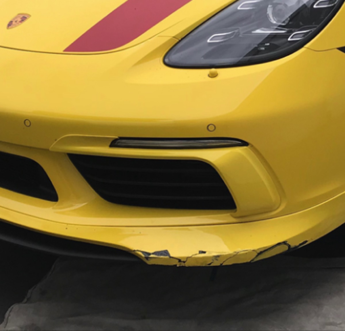 Bumper Crack Repair before in Orange, CA, Cracked and chipped front bumper lip on a Porsche 718, rebuilt, refinished, and color-matched on-site in Orange County.