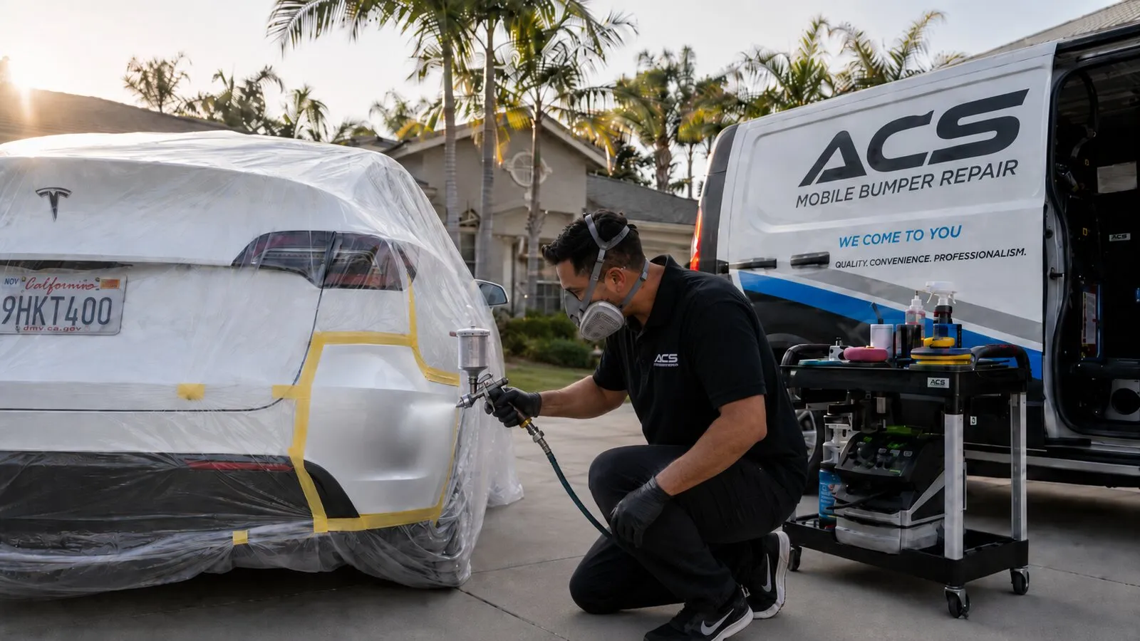 ACS technician spray-painting a masked-off white Tesla rear bumper with an exact PPG color match, the ACS we-come-to-you mobile van in the driveway in Orange County